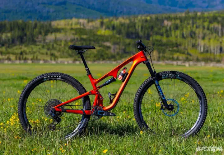 An orange Revel Ranger V2 mountain bike sits in a grassy field, ready for adventure. This revel ranger v2 review shows its sleek design.