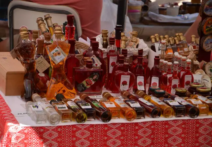 Różnorodne butelki z rakiją, w tym te w kształcie kobiecym, oferowane na targu. Co to rakija? To tradycyjny alkohol, często owocowy.