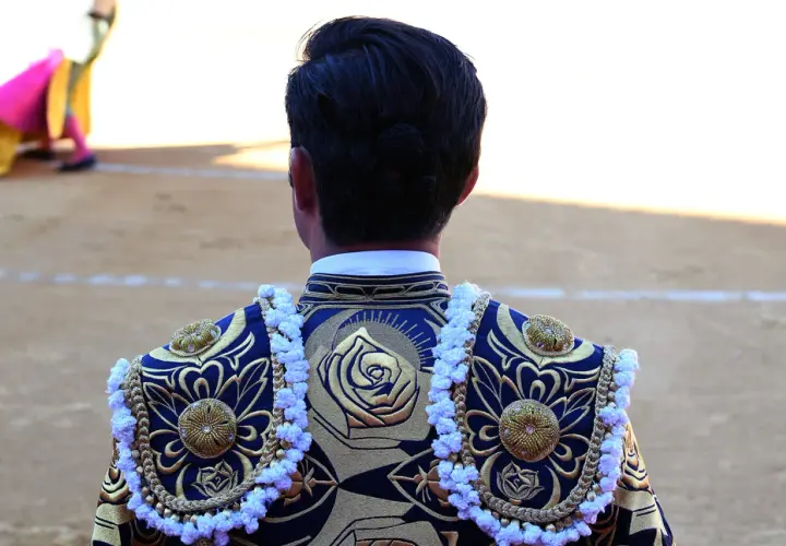 Detalle de la espalda de un torero con bordados dorados y azules, mostrando los vibrantes colores taurinos.
