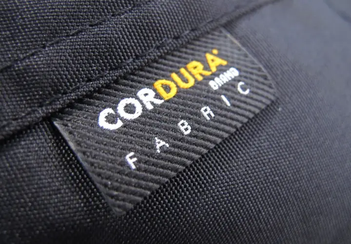 Czarna tkanina z naszywką "CORDURA FABRIC". Materiał ten, znany ze swojej wytrzymałości, często wykorzystywany jest w produktach outdoorowych, jak plecaki czy torby.
