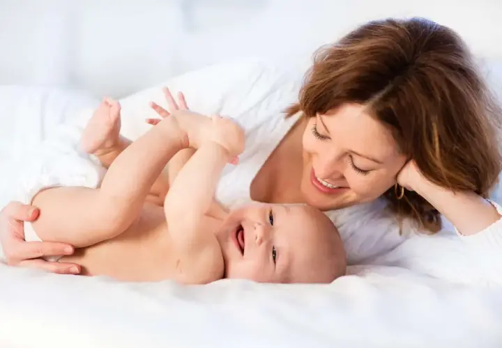 Uśmiechnięta mama patrzy na radosne dziecko leżące na białym tle.