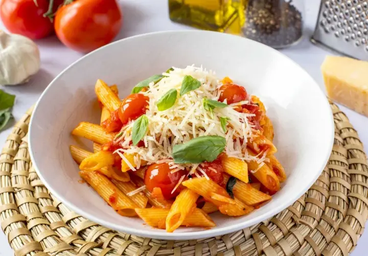 Un plato de macarrones a la napolitana, con salsa de tomate, tomates cherry, albahaca fresca y queso rallado.