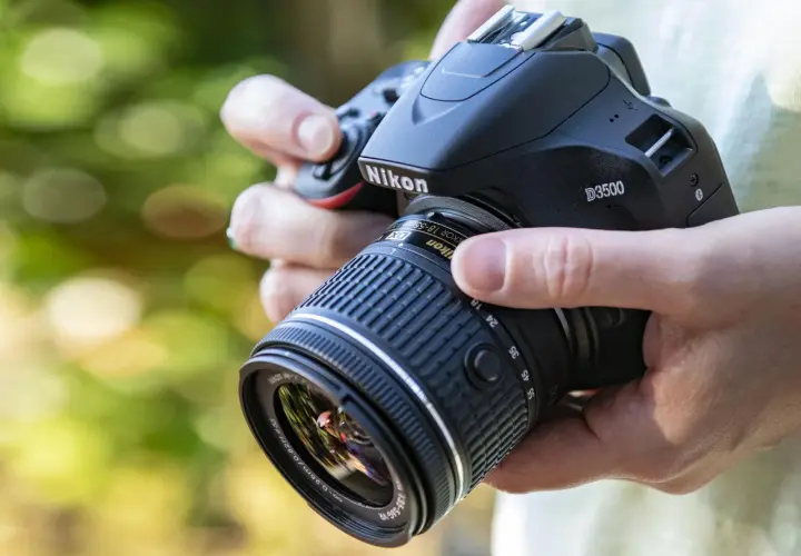 Mani che impugnano una Nikon D3500 con obiettivo 18-55mm. Dettagli sulla nikon d3500 scheda tecnica.