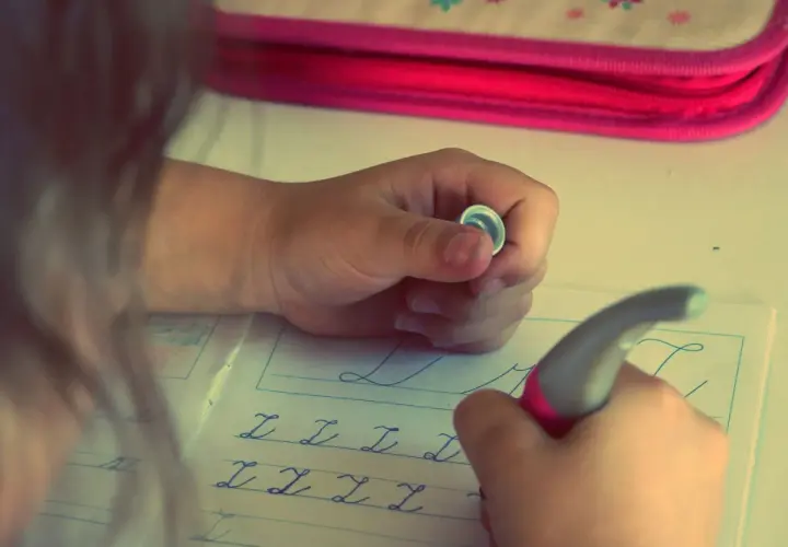 Niño/a practicando caligrafía en un cuaderno con letras cursivas.