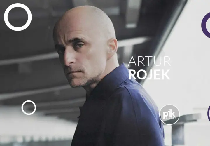 Artur Rojek, znany z energetycznych koncertów, na tle miejskiego krajobrazu.