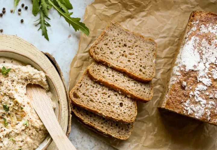 Chleb żytni, pokrojony w kromki, obok miski z pastą. Czy żyto ma gluten? Tak, żytnie pieczywo zawiera gluten.