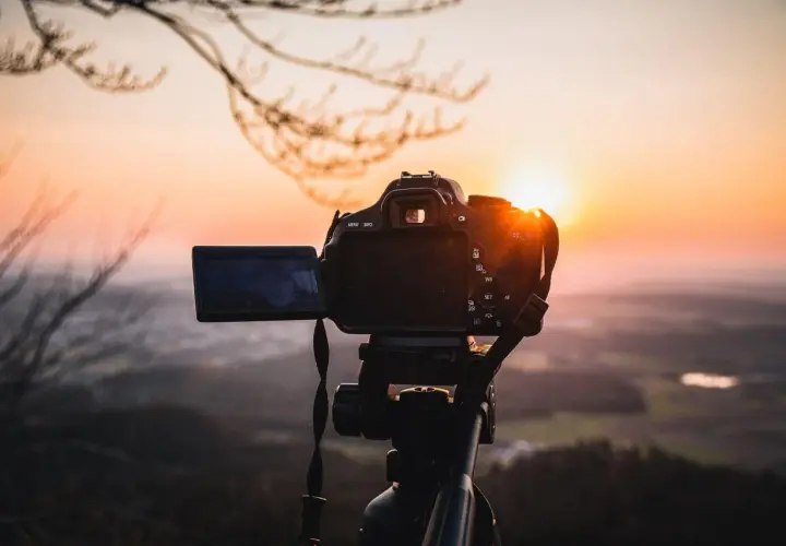 Aparat fotograficzny na statywie, gotowy do uchwycenia zachodzącego słońca nad doliną. Solidna podstawa aparatu zapewnia stabilność.