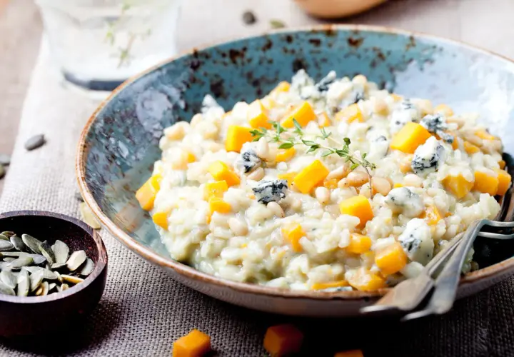 Cremiges Kürbis-Risotto mit Blauschimmelkäse und Pinienkernen. Ein Glas Wasser steht bereit, perfekt zum Genießen dieses Risotto, welcher Wein passt wohl dazu?