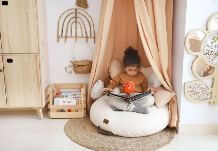 Niña en un acogedor montessori rincón de lectura niños, absorta en un libro pop-up.
