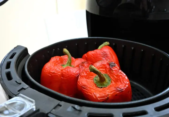 Peperoni rossi interi cotti nella friggitrice ad aria, con la buccia leggermente raggrinzita e qualche macchia scura.