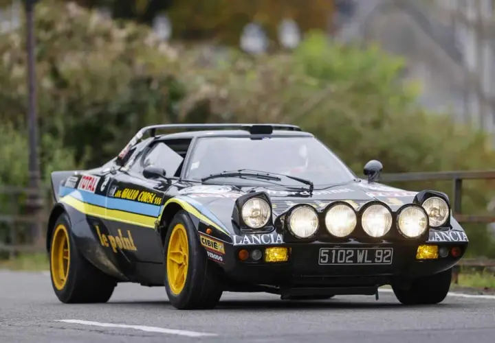Czarny Lancia Stratos z żółtymi felgami i rajdowymi oznaczeniami, gotowy do pokonania kolejnego zakrętu.