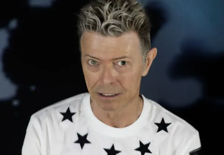 Ikoniczny David Bowie w 2016 roku, w białej koszulce w czarne gwiazdy, z charakterystyczną fryzurą.