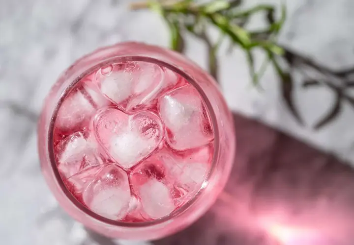 En rosa drink med hjärtformade isbitar och en rosmarinkvist.