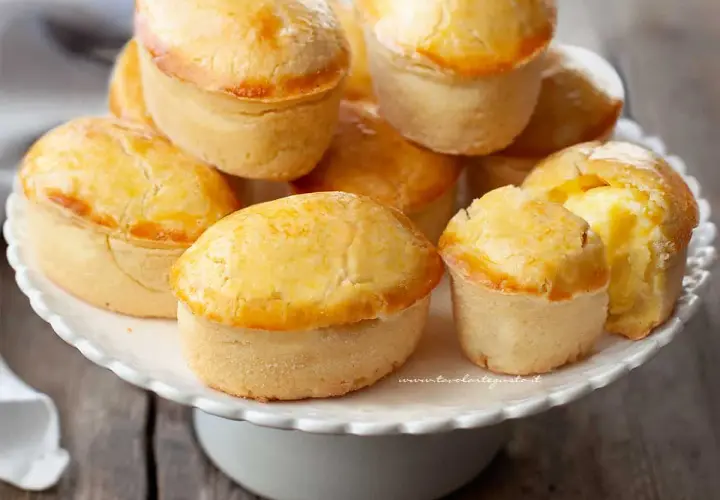 Un mucchio di pasticciotti leccesi dorati e invitanti su un'alzata bianca, pronti per essere gustati.