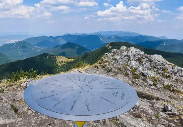 Widok z klak szczyt na pasmo górskie. Na pierwszym planie metalowa tablica z nazwami szczytów.