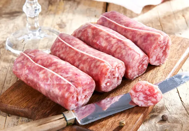 Frische Salsiccia-Würste auf Holzbrett, Messer mit Scheibe. Die korrekte Salsiccia Aussprache ist wichtig für den Genuss.