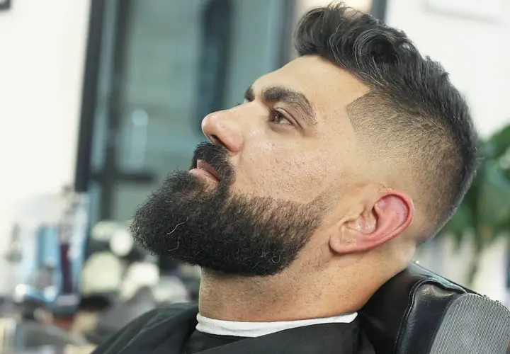 Hombre con barba y un moderno corte de pelo con degradado, uno de los tipos de corte de pelo hombre más populares.