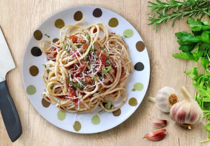 Un plato de espagueti aglio olio peperoncino, con ajo, perejil y un toque de tomate.