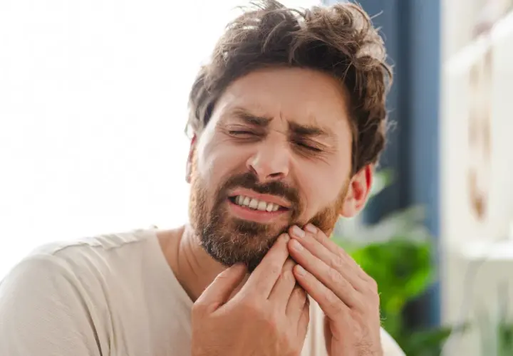 Hombre con expresión de dolor, tocándose la mejilla por una caries muela.