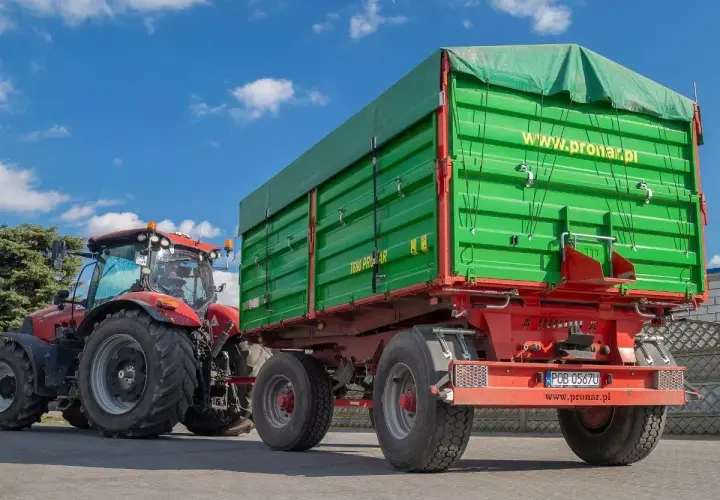 Czerwony traktor ciągnie zieloną przyczepę. Dowiedz się, jakich przyczep nie trzeba rejestrować, by ułatwić sobie pracę w gospodarstwie.