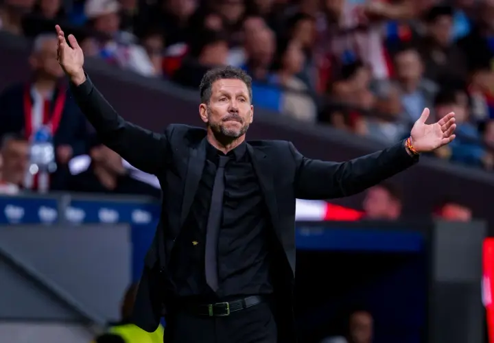 Diego Simeone, trener Atletico, w czarnym garniturze z rozłożonymi rękami, gestykuluje na boisku.