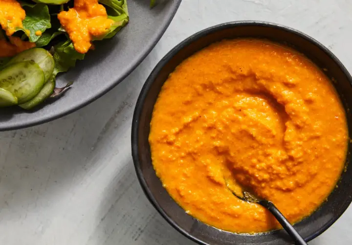 A vibrant bowl of carrot ginger dressing sits next to a salad with cucumber slices.