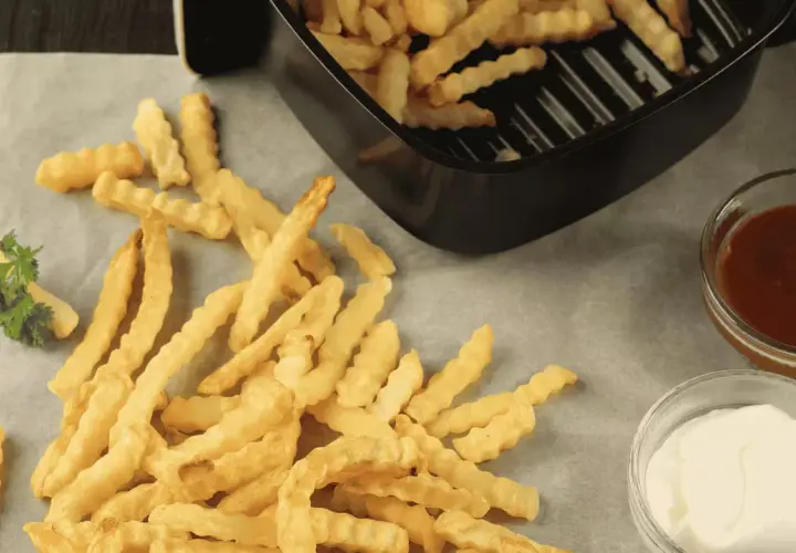 Frites maison ondulées, croustillantes et dorées, tout juste sorties de l'airfryer Ninja. Servies avec ketchup et mayonnaise.