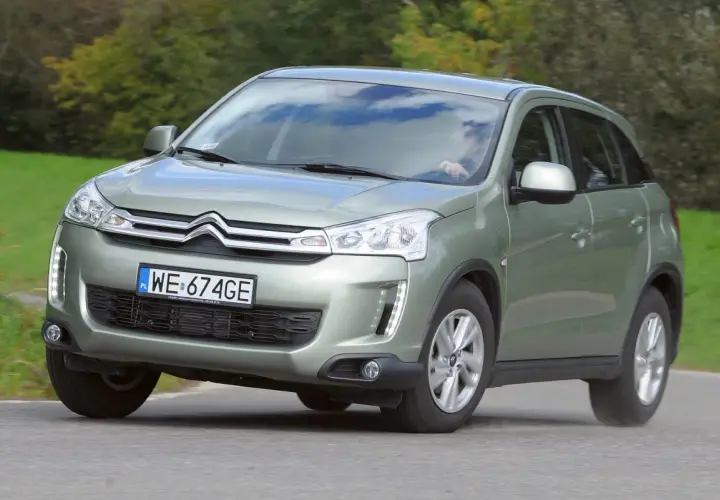 Zielony Citroën C4 Aircross z polskimi tablicami WE 674GE jedzie po drodze wśród zieleni.