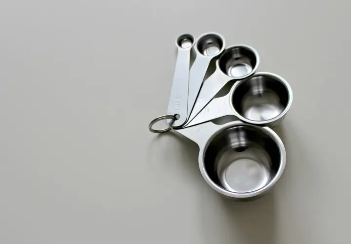 Zestaw metalowych miarek kuchennych o różnych rozmiarach, ułożonych na jasnym tle.