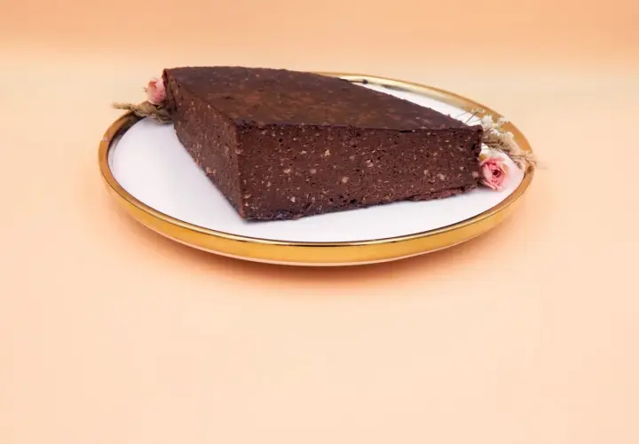 Czekoladowy brownie z bananami i masłem orzechowym, ozdobione suszonymi kwiatami, na talerzu ze złotym rantem.