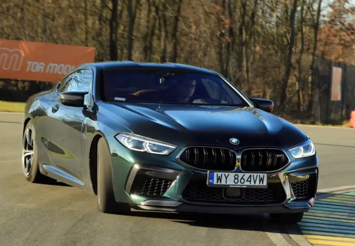 Mocne m8 bmw w ciemnozielonym kolorze na torze wyścigowym, z widocznym banerem "TOR MODLIN" w tle.