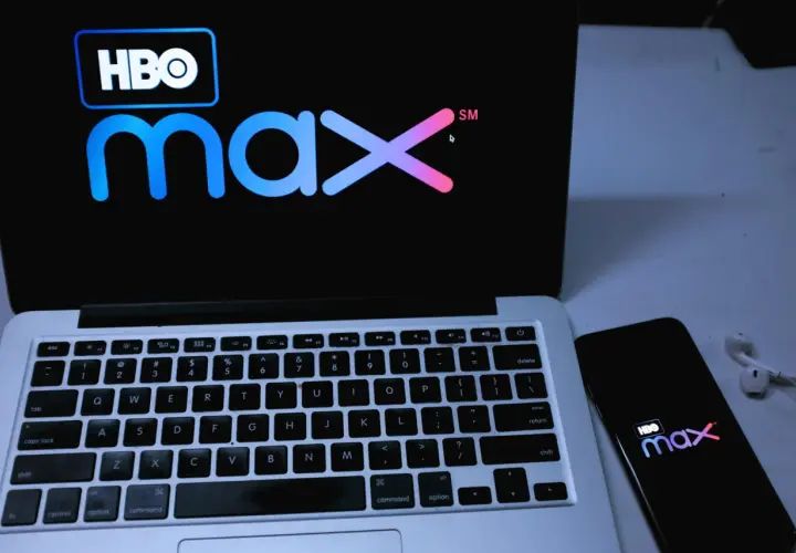 Logo HBO Max na ekranie laptopa i smartfona, obok słuchawki.