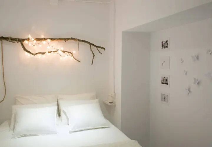 Ideas para decorar ramas secas: una rama con luces cálidas sobre la cama, fotos y mariposas en la pared.