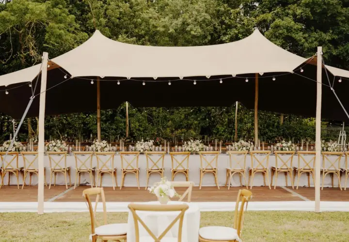 Une réception de mariage sous tente, avec des tables dressées et des chaises en bois. Un travail de cout wedding planner pour un événement mémorable.
