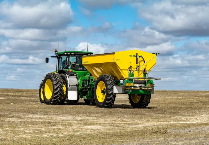 Zielony John Deere 7810 z żółtym rozsiewaczem Landaco T130 na polu.
