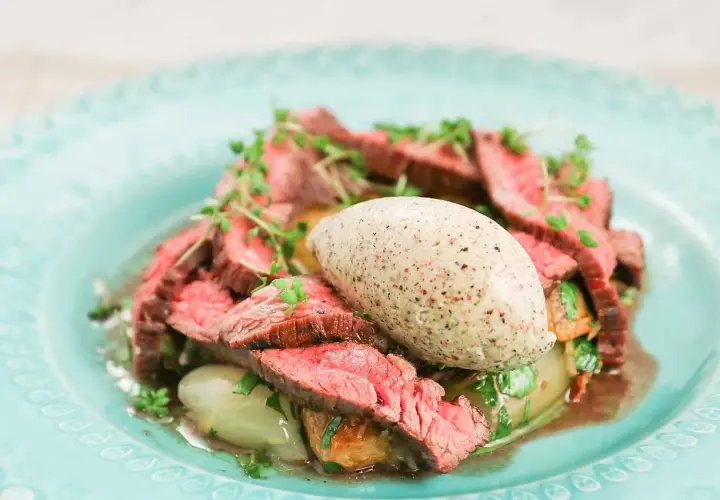 Skivad flankstek Morberg med potatis och en klick potatispuré, garnerad med örter.