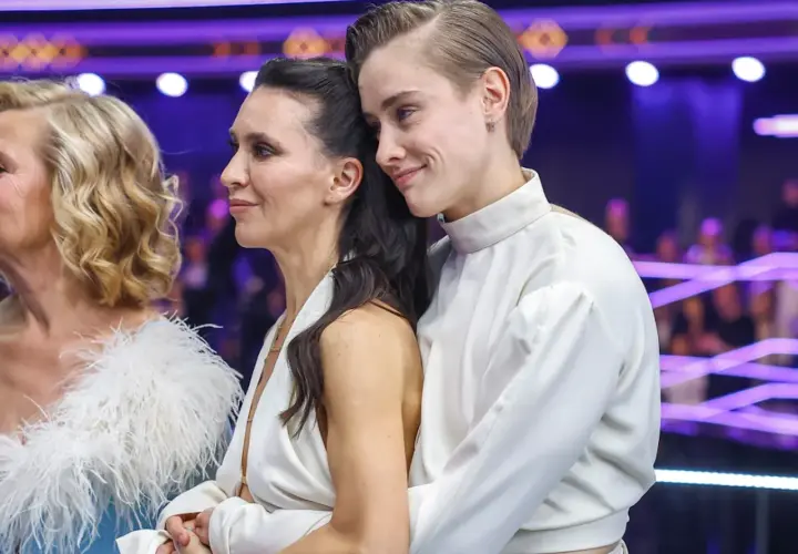 Katarzyna Zillmann i jej partnerka w białych strojach, czule objęte, na tle fioletowych świateł.