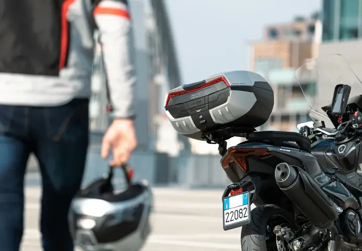 Hombre con casco en mano, listo para llevar su maleta en moto. La moto tiene un top case Givi Maxia.