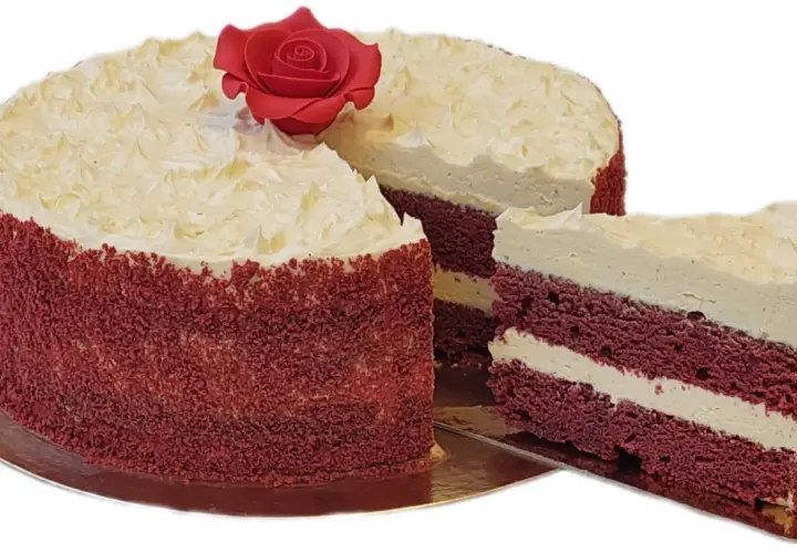 Un delicioso bizcocho red velvet con cobertura cremosa y una rosa roja decorativa. Una rebanada muestra sus capas rojas y blancas.