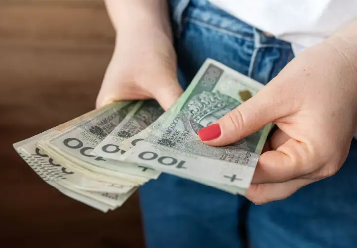 Dłonie trzymające stos banknotów 100 zł. Czy to przyszła kwota bazowa służba cywilna 2026?