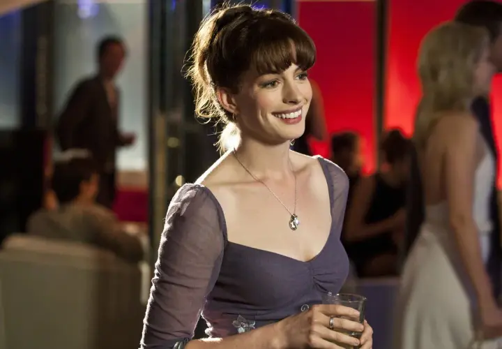 Anne Hathaway w filmie, uśmiechnięta, trzymająca drinka.