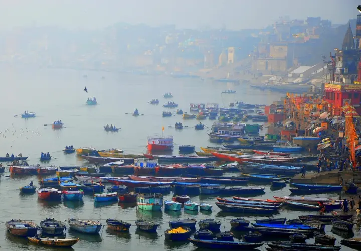 Tłum łodzi na rzece Ganges, z miastem w tle.