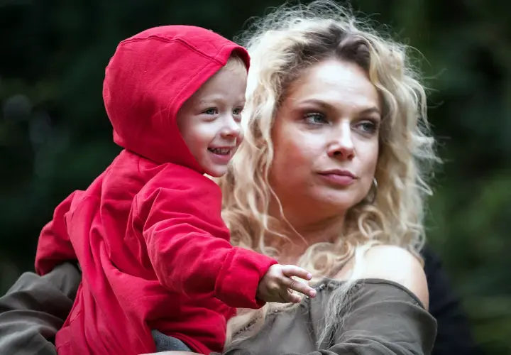 Joanna Liszowska z dziećmi, uśmiechnięty chłopiec w czerwonej bluzie na rękach mamy.