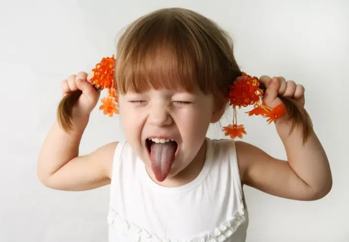 Bambina iperattiva fa una smorfia con la lingua fuori, tirando le trecce con fiori arancioni. Cosa fare?