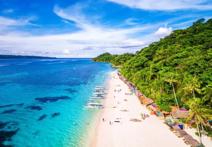 Piękna plaża na Filipinach, gdzie turkusowa woda i biały piasek tworzą rajski widok. Nawet podczas pory deszczowej, słońce przebija się przez chmury, zapraszając do relaksu.