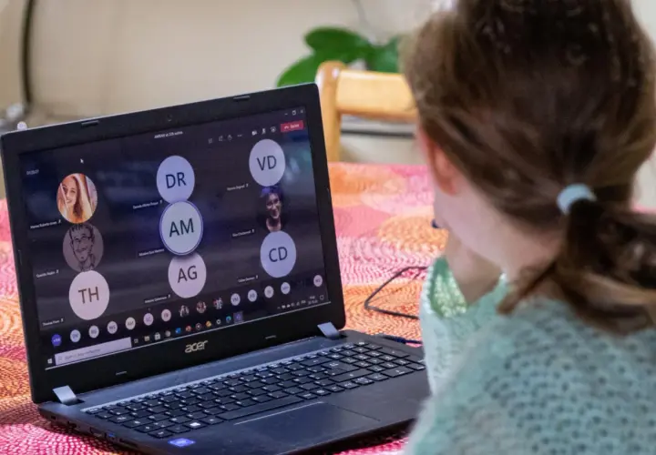 Dziewczynka uczestniczy w lekcji online przez msteams. Na ekranie laptopa widać wiele okręgów z inicjałami uczestników.