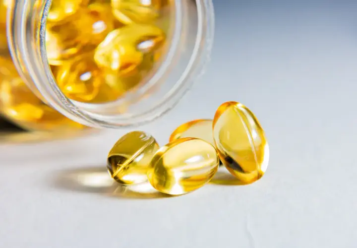 Żółte kapsułki z kwasy omega 3 wysypują się ze słoiczka.