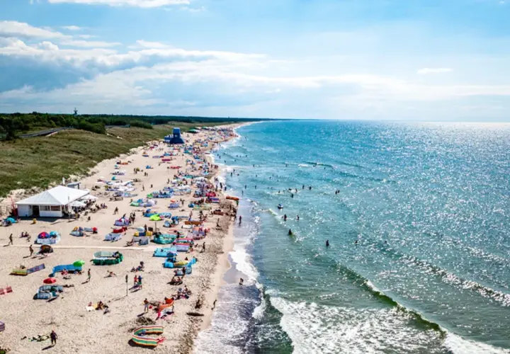 Tłum ludzi na plaży w Darłowie, korzystających z uroków lata. Wiele kolorowych parawanów i namiotów, a w wodzie kąpielowicze. To wspaniałe darłowo atrakcje.