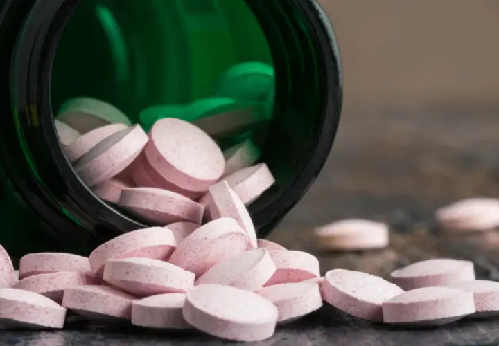 Różowe tabletki wysypują się z zielonego pojemnika. Wśród nich widać tabletki z chromem, które mogą pomóc w utrzymaniu prawidłowego metabolizmu.