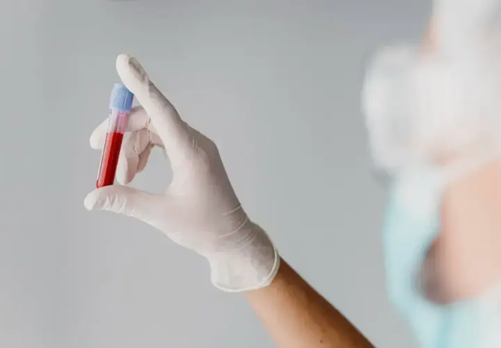 Ręka w białej rękawiczce trzyma probówkę z krwią, gotową do podstawowych badań krwi.